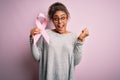 Young african american afro girl holding pink cancer ribbon over isolated background screaming proud and celebrating victory and Royalty Free Stock Photo