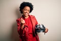 Young African American afro motorcyclist woman with curly hair holding motorcycle helmet Beckoning come here gesture with hand