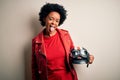 Young African American afro motorcyclist woman with curly hair holding motorcycle helmet sticking tongue out happy with funny