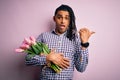 Young african american afro romantic man with dreadlocks holding bouquet of pink tulips Surprised pointing with hand finger to the