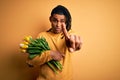 Young african american afro romantic man with dreadlocks holding bouquet of yellow tulips Pointing with finger up and angry Royalty Free Stock Photo