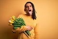 Young african american afro romantic man with dreadlocks holding bouquet of yellow tulips sticking tongue out happy with funny Royalty Free Stock Photo