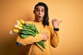 Young african american afro romantic man with dreadlocks holding bouquet of yellow tulips Surprised pointing with hand finger to