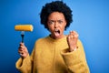 Young African American afro vegetarian woman with curly hair holding fork with cob corn annoyed and frustrated shouting with