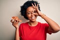 Young African American afro woman with curly hair eating slice of delicious Italian pizza with happy face smiling doing ok sign Royalty Free Stock Photo