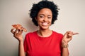 Young African American afro woman with curly hair eating slice of delicious Italian pizza very happy pointing with hand and finger Royalty Free Stock Photo