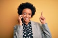 Young African American afro woman with curly hair having conversation talking on smartphone surprised with an idea or question Royalty Free Stock Photo