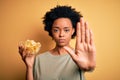 Young African American afro woman with curly hair holding bowl with chips potatoes with open hand doing stop sign with serious and