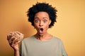Young African American afro woman with curly hair holding bowl with cornflakes cereals scared in shock with a surprise face,