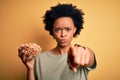 Young African American afro woman with curly hair holding bowl with salty peanuts pointing with finger to the camera and to you, Royalty Free Stock Photo