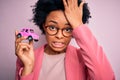 Young African American afro woman with curly hair holding car toy over pink background stressed with hand on head, shocked with Royalty Free Stock Photo