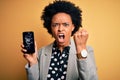 Young African American afro woman with curly hair holding cracked broken smartphone annoyed and frustrated shouting with anger,