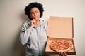Young African American afro woman with curly hair holding delivery box with Italian pizza serious face thinking about question, Royalty Free Stock Photo