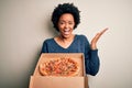 Young African American afro woman with curly hair holding delivery box with Italian pizza very happy and excited, winner Royalty Free Stock Photo