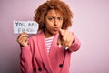 Young African American afro woman with curly hair holding papaer with you are fired message pointing with finger to the camera and Royalty Free Stock Photo