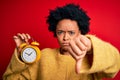 Young African American afro woman with curly hair holding vintage alarm clock with angry face, negative sign showing dislike with Royalty Free Stock Photo