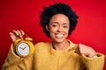 Young African American afro woman with curly hair holding vintage alarm clock with surprise face pointing finger to himself Royalty Free Stock Photo