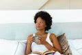 Young african american afro woman looking away while sitting with coffee cup and book on bed Royalty Free Stock Photo