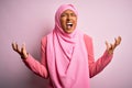Young African American afro woman wearing muslim hijab over isolated pink background crazy and mad shouting and yelling with Royalty Free Stock Photo