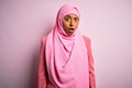 Young African American afro woman wearing muslim hijab over isolated pink background In shock face, looking skeptical and