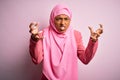 Young African American afro woman wearing muslim hijab over isolated pink background Shouting frustrated with rage, hands trying Royalty Free Stock Photo