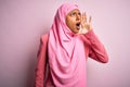 Young African American afro woman wearing muslim hijab over isolated pink background shouting and screaming loud to side with hand Royalty Free Stock Photo