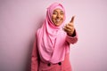 Young African American afro woman wearing muslim hijab over isolated pink background smiling friendly offering handshake as Royalty Free Stock Photo