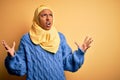 Young African American afro woman wearing muslim hijab over isolated yellow background crazy and mad shouting and yelling with Royalty Free Stock Photo
