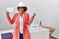 Young african american architect woman at political election holding envelope screaming proud, celebrating victory and success Royalty Free Stock Photo