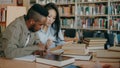 Young african american and asian college students working together preparing for exams while sitting at table at Royalty Free Stock Photo