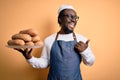 Young african american bakery man holding tray with healthy wholemeal bread pointing and showing with thumb up to the side with Royalty Free Stock Photo