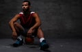 Young African-American basketball player in sportswear sitting on a ball on a dark background. Royalty Free Stock Photo