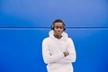 Young African American black man listening music with wireless headphones while wearing a white sweatshirt, looking to camera with Royalty Free Stock Photo