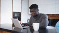 Young african american black man working on laptop in his appartment and drinking tea or coffee Royalty Free Stock Photo