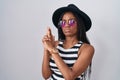 Young african american with braids wearing hat and sunglasses holding symbolic gun with hand gesture, playing killing shooting