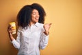 Young african american business woman with afro hair drinking coffee from take away cup pointing and showing with thumb up to the Royalty Free Stock Photo