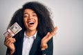 Young african american business woman with afro hair holding a bunch of cash dollars banknotes very happy and excited, winner Royalty Free Stock Photo