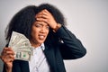 Young african american business woman with afro hair holding cash dollars banknotes stressed with hand on head, shocked with shame Royalty Free Stock Photo