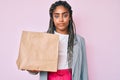 Young african american business woman with braids holding take away paper bag thinking attitude and sober expression looking self Royalty Free Stock Photo