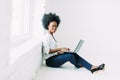 Young african american business woman using the laptop, while sitting on the floor near a big window in studio Royalty Free Stock Photo