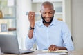 Young african american businessman on a call using a phone while reading a note in a notebook and working on a laptop in Royalty Free Stock Photo