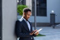 Young african american businessman in formal business suit standing working with tablet in hands on background modern office Royalty Free Stock Photo