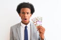 Young african american businessman holding dollars standing over isolated white background scared in shock with a surprise face, Royalty Free Stock Photo