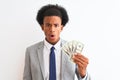 Young african american businessman holding dollars standing over isolated white background scared in shock with a surprise face, Royalty Free Stock Photo