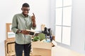 Young african american businessman unboxing box at the office beckoning come here gesture with hand inviting welcoming happy and Royalty Free Stock Photo