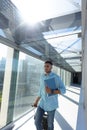 Young african american businessman walking with file and luggage at airport corridor on sunny day Royalty Free Stock Photo