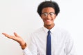 Young african american businessman wearing tie and glasses over isolated white background smiling cheerful presenting and pointing Royalty Free Stock Photo