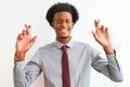 Young african american businessman wearing tie standing over isolated white background gesturing finger crossed smiling with hope