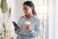 Young african american businesswoman using her phone while drinking a coffee alone in an office at work. One black woman Royalty Free Stock Photo