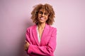 Young african american businesswoman wearing glasses standing over pink background happy face smiling with crossed arms looking at Royalty Free Stock Photo